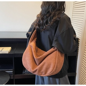 Close-up of a large crescent crossbody bag in brown suede fabric worn over the shoulder