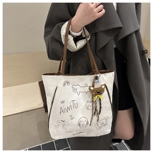 Detail of canvas tote bag with brown straps featuring whimsical illustrations and bear charm
