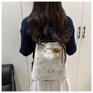 Detail of white canvas backpack featuring cartoon graffiti and cute bear plush charm