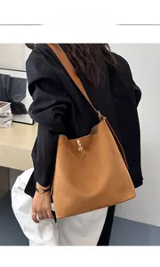 Brown suede tote bag with golden buckle shown on shoulder of a model in a modern setting