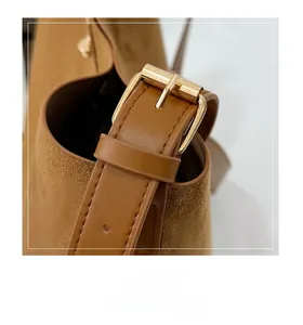 Detail of light gold metal adjustment buckle on a brown suede shoulder bag