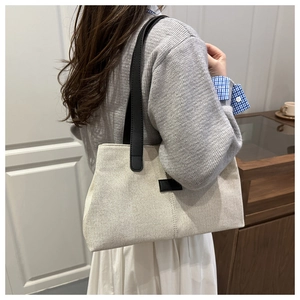 Close-up of cream canvas tote bag with black leather straps shown in a cozy interior