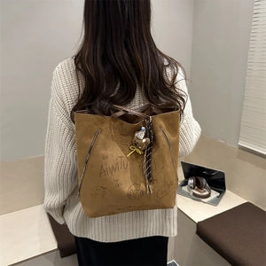 Brown faux suede tote bag with cartoon illustration and teddy bear charm on model