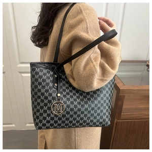 Detail of grey monogram tote bag with gold M-shaped metal pendant and leather strap