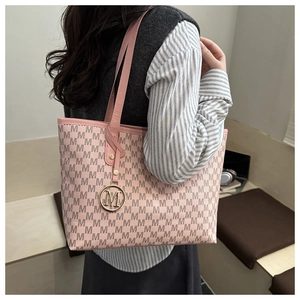 Side view of a pink tote bag with brown M patterns and gold charm on a female model