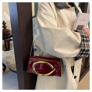 Detail of burgundy patent leather shoulder bag featuring a large gold oval buckle and chain