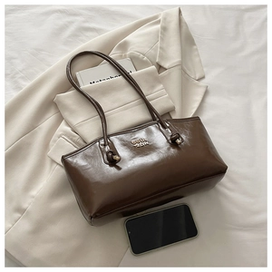 Detail of dark brown glossy shoulder bag with metal logo and knot on soft white background