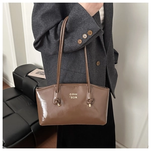 Brown leather tote bag featuring gold lettering and knotted strap details worn with a suit