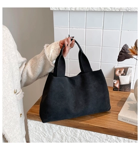 Detail of minimalist black suede tote bag with wide strap for winter chic styling