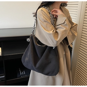 Detail of black corduroy tote bag with striped woven strap and decorative knot accents