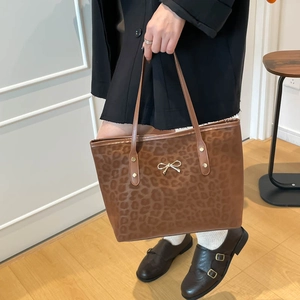 Brown leopard print tote bag with golden bow accessory shown in a modern interior setting