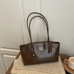 Dark brown high-gloss tote bag with metal logo on a cozy knit and wood background