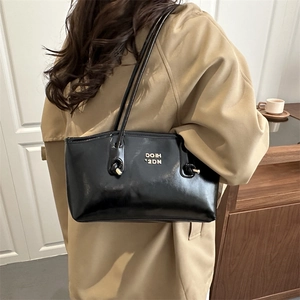 Fashionable black glossy shoulder bag for women with gold lettering and minimalist design