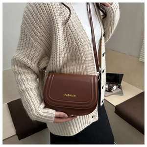 Detail shot of a brown leather saddle bag with gold lettering and adjustable shoulder strap