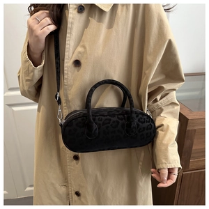 Chic black leopard print cylindrical crossbody bag styled on a beige trench coat