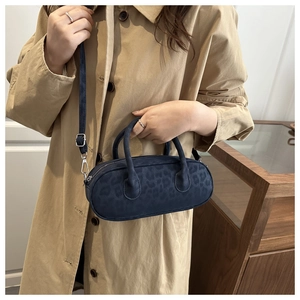 Dettaglio della borsa cilindrica blu navy con stampa leopardata abbinata a un trench coat