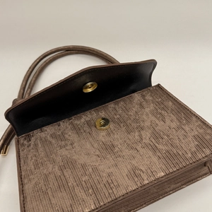 Detail van bronzen getextureerde handtas met gouden magneetsluiting en metallic stof