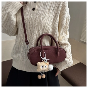 Close-up of burgundy cylindrical leather crossbody bag with cute teddy bear charm