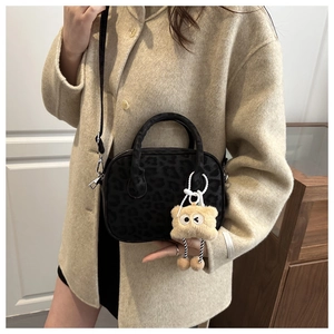 Detail of leopard print textured handbag featuring a cute plush monster charm accessory
