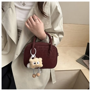 Detail van bordeauxrode crossbodytas met pluchen koekjeshanger en stijlvolle handvaten