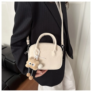 Close-up of a beige matte shoulder bag with a brown plush charm on a model's arm