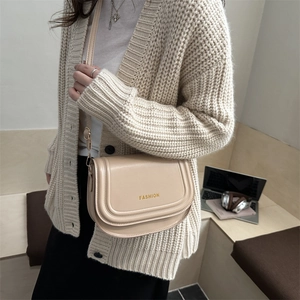 Fashionable cream faux leather saddle bag with shoulder strap shown in a lifestyle setting