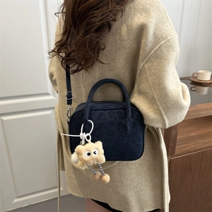 Navy leopard embossed handbag with plush charm shown on a beige coat model