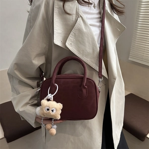 Minimalist burgundy suede handbag with teddy bear charm and sleek shoulder strap