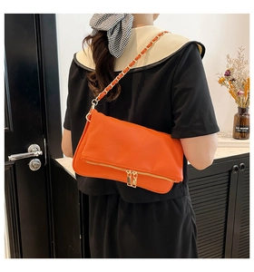Detail of orange pebble leather crossbody bag with decorative gold zipper and chain strap