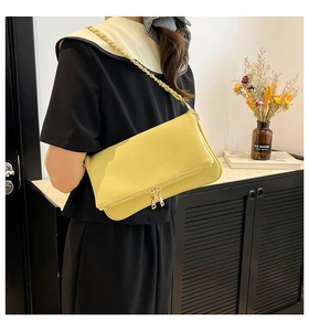 Close-up of bright yellow leather shoulder bag with golden chain and dual zippers