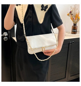 Detail of white leather crossbody bag with gold zipper and metal chain strap on a model