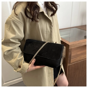 Detail of matte black chain bag held by model wearing a classic khaki trench coat