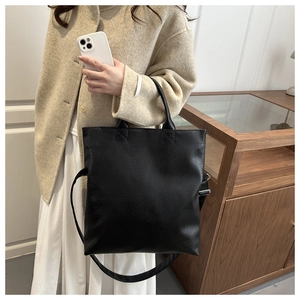 Dettaglio borsa tote nera testurizzata indossata con cappotto beige e tracolla