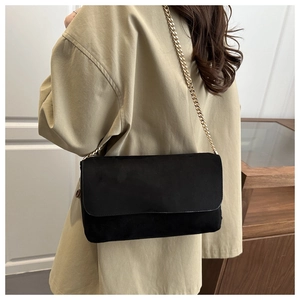 Detail of a minimalist black suede shoulder bag with light gold metal chain strap on model