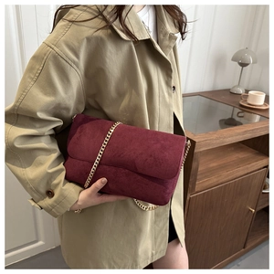 Detail of maroon suede crossbody bag with gold chain strap on a trench coat