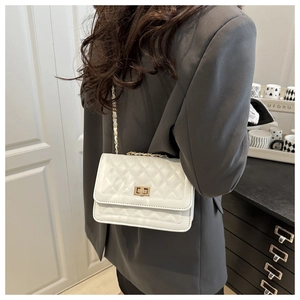 Détail d'un sac matelassé blanc avec chaîne dorée porté sur un blazer gris