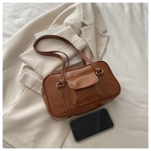 Brown patent leather shoulder bag with contrast stitching and pocket next to a phone for scale
