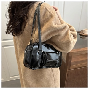 Detail of glossy black shoulder bag featuring white contrast stitching and mini front pocket