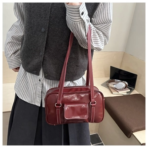 Detail of dark red glossy shoulder bag with white stitching and front pocket on a model