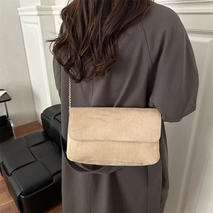 Beige suede crossbody bag with gold chain strap shown on a model in a minimalist setting