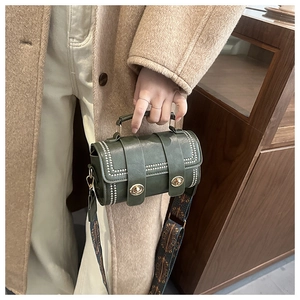 Detail of dark green barrel bag with white studs and ethnic style wide woven strap