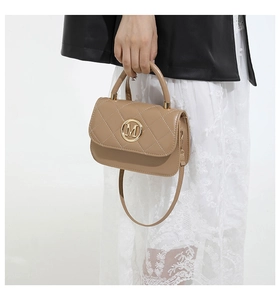 Gros plan du sac beige matelassé avec logo M doré et poignée porté par un mannequin
