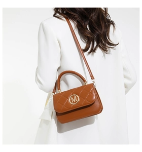 Détail du sac matelassé marron avec boucle M sur un mannequin en blazer blanc