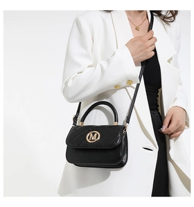 Gros plan du sac à bandoulière en cuir matelassé avec logo M doré sur un blazer blanc