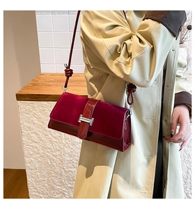 Close-up of burgundy shoulder bag with silver H-buckle on stylish trench coat