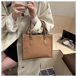 Brown embossed tote bag with clover pattern held by a model in a cozy city cafe setting