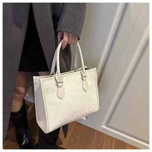 Detail of white square tote bag featuring embossed clover patterns and sturdy handles