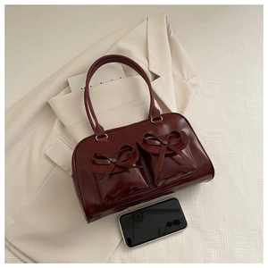 Detail of dark red glossy leather bowling bag featuring front pockets and decorative bows