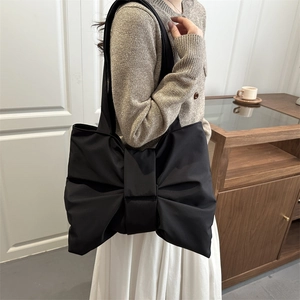 Black bow-shaped oversized tote bag in soft nylon shown on a model in a stylish interior