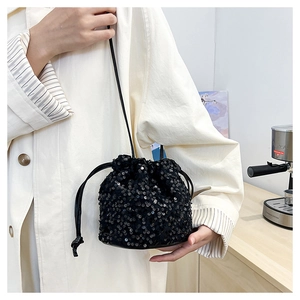 Detail of black sequin drawstring bucket bag with leather strap on a model